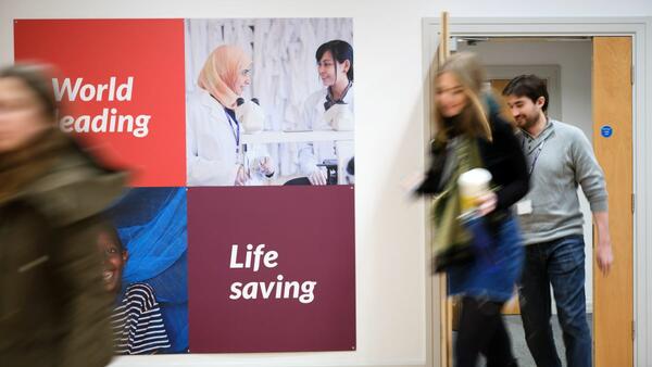 Students at LTSM walking through a door. On the wall, a poster says 'Life Saving', 'World Changing'