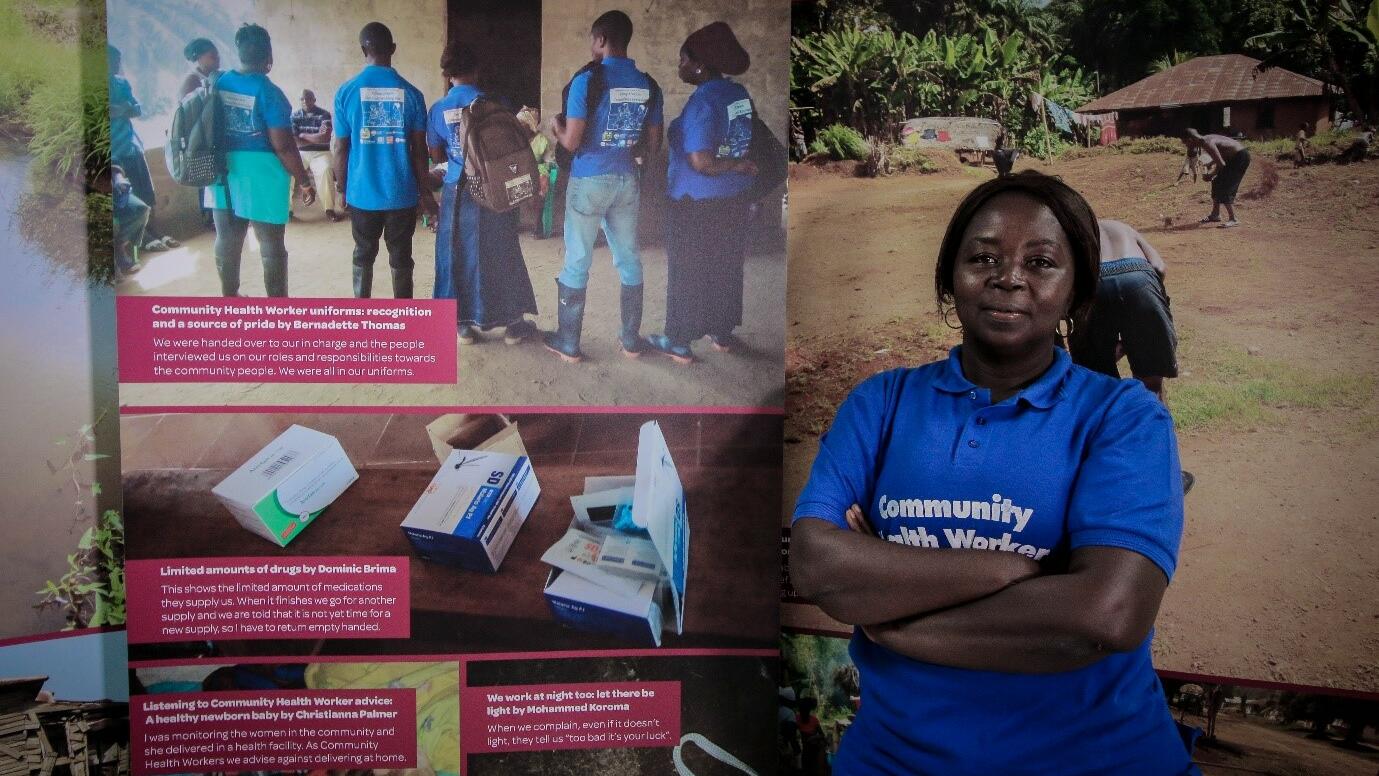 Bernadette Thomas a Community Health Worker from Bonthe District of Sierra Leone poses next to a photo exhibition about the challenges she and her colleagues face in the course of their work. Bernadette Thomas a Community Health Worker from Bonthe District of Sierra Leone poses next to a photo exhibition about the challenges she and her colleagues face in the course of their work.